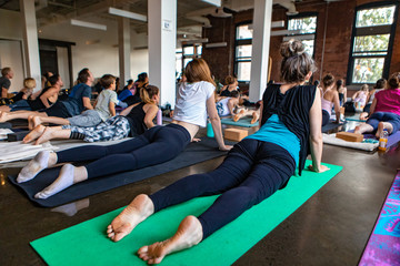 Fototapeta na wymiar Diverse group of people in yoga class. People are seen lying on gym mats and doing the upward facing dog pose during 108 salutations to the sun. A spiritual set of posture poses.