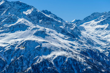 A rescue helicopter in the high mountains. Tall Alps surrounding the vehicle that is getting ready to land. Mountains slopes are covered with thick snow. Dangerous rescue mission.