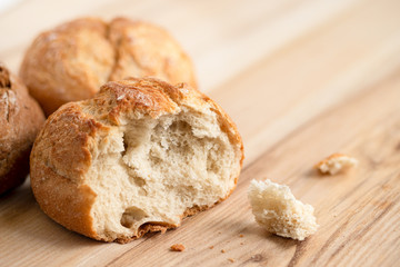 Broken round rustic white bread roll next to two round bread rolls on light wood.