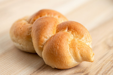 Plaited plain white bread roll isolated on light wood.