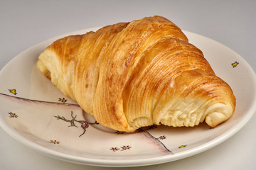 Gros plan sur un croissant dans sa petite assiette et fond blanc
