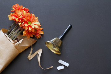 School bell and chalk on blackboard with flowers teacher day abstract background