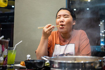 Happy chubby Asian woman holding chopsticks enjoying to eat in Japanese Shabu restaurant