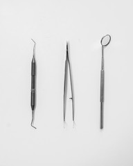 Dentist table with tools on a white background top view. A mirror, tweezers and a probe are on the doctors table. Oral hygiene, caries prevention, examination.