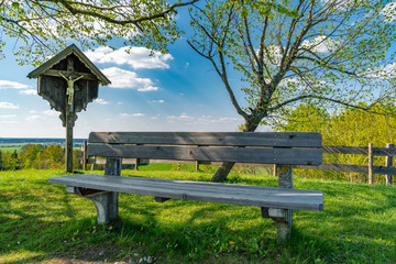 Holzbank neben einem Wegkreuz in einer idyllischen Landschaft