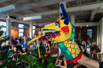 Naklejka premium Diverse group of people in yoga class. A close up and side profile view of a hand puppet on the arm of a person, a colorful and fun dragon's head used to motivate people during grueling gym workout.