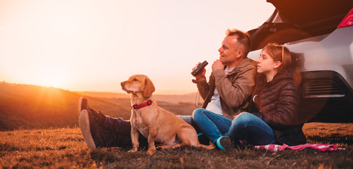 Father and daughter with dog camping on a hill while sitting by the car