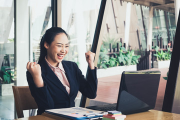 Business woman euphoric watching a laptop on a desk winning at modern office