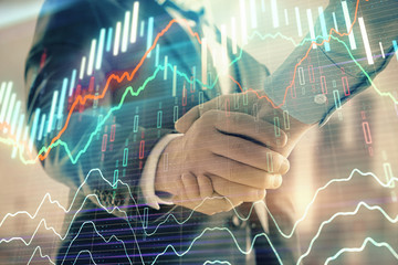 Double exposure of financial graph on cityscape background with two businessman handshake. Concept of stock market deal