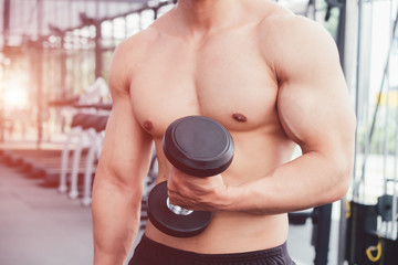 Fototapeta na wymiar Muscular bodybuilder Man holding rows of dumbbells showing muscular body and sixpack abs at a gym