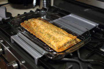 Baked cedar plank salmon on a glass baking tray resting on the stove top.