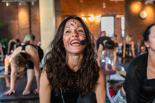 Diverse group of people in yoga class. A motivational gym instructor is seen from the front in lying cobra pose during 108 salutations to the sun. Wearing mic to guide people through grueling workout