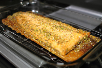 Baked cedar plank salmon on a glass baking tray resting on the stove top.