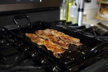 Korean style BBQ short ribs, known as Kalbi, on a carbon steel griddle in a home kitchen.