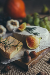 Camembert and Munster cheese with figs, nuts, grapes, rosemary, garlic and other vegatables on wooden table. Copyspace included.