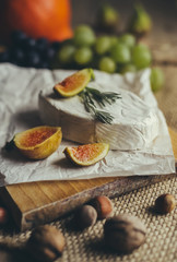 Camembert and Munster cheese with figs, nuts, grapes, rosemary, garlic and other vegatables on wooden table. Copyspace included.