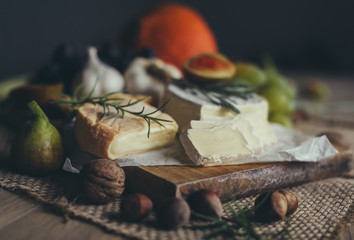 Camembert and Munster cheese with figs, nuts, grapes, rosemary, garlic and other vegatables on wooden table. Copyspace included.