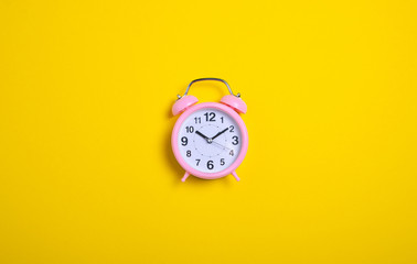 Modern pink alarm clock on yellow background, top view