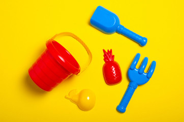 Baby set red sandbox bucket shovel rake toy on yellow background, top view