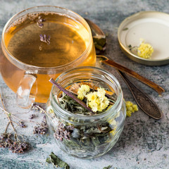 Herbal tea from medicinal plants (Helichrysum flowers, oregano grass, buckthorn bark) in a glass mug on an old table.  Selective focus.