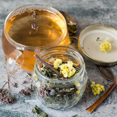 Herbal tea from medicinal plants (Helichrysum flowers, oregano grass, buckthorn bark) in a glass mug on an old table.  Selective focus.