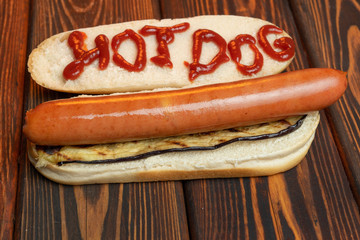 Hot dog bun with Bratwurst sausages and fried eggplant on electric barbecue on dark background. Text ketchup Hot-dog on bread. Top view. Close-up