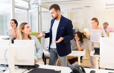 Upset girl sitting at laptop in coworking space while dissatisfied businessman pointing out mistakes in her work