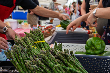 Organic produce at a farmer's market. Nutrient rich asparagus is seen in bunches on a market stall, blurry traders and customers are seen in the background with room for copy.