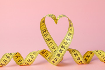 Yellow measuring tape in the shape of a heart on a pink background. The concept of weight loss for...