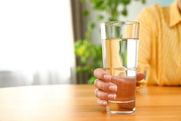 Woman holding glass of water at wooden table, closeup with space for text. Refreshing drink