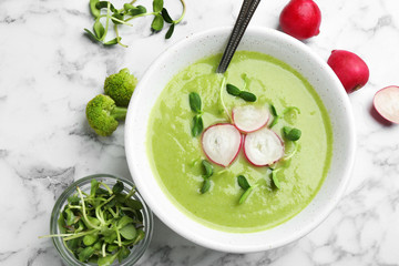 Flat lay composition with bowl of broccoli cream soup on white marble table