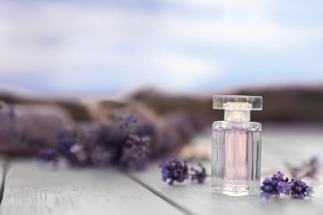 Bottle of luxury perfume and lavender flowers on white wooden table outdoors. Space for text