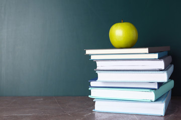 Books and apple on grey table near chalkboard, space for text. School education