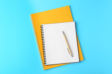 Notebooks and pen on light blue background, top view