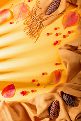 Autumn composition with yellow scarf or blanket, leaves, red berries, pine cones on sunny yellow background