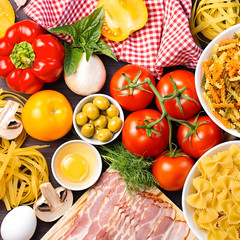 Italian food ingredients - pasta, vegetables, mushrooms, bacon, eggs, olives. Flat lay on dark wooden background