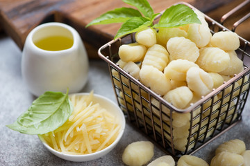 Uncooked potato gnocchi with grated parmesan cheese, olive oil and fresh green basil, close-up, selective focus
