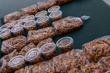 Organic produce at a farmer's market. A close up view of plastic bags and small pots filled with roasted cashew nuts, for sale on a market stall during a local food and cottage industry fair.