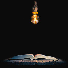 Old opened book and lamp hanging above isolated on black background