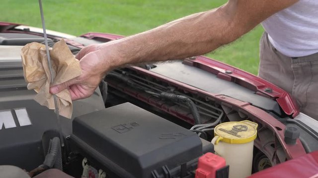 Man checking engine oil in vehicle, car mechanic at work under the hood.