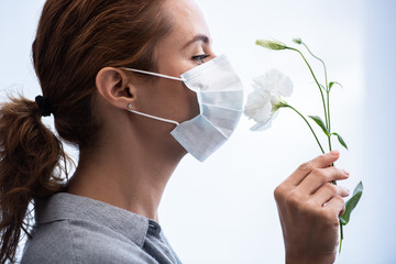 side view of woman in medical mask smelling flowers - obrazy, fototapety, plakaty