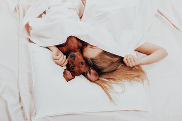 Beautiful girl lying relax in bed with her beloved dog. morning prodding in a warm comfortable bed....