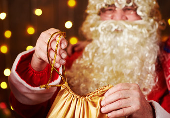 Santa Claus opens a bag of gifts, sitting indoor near decorated xmas tree with lights - Merry Christmas and Happy Holidays!