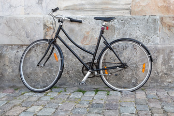 Fototapeta na wymiar Plain black bike leaning against a marble wall in a cobblestone street.