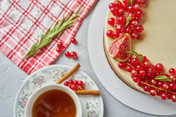 Round homemade cake decorated with red currants, figs, cinnamon and rosemary with tablecloth, Cup and saucer on a light background concrete table.