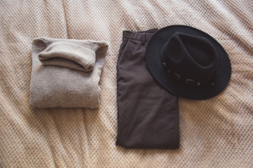 folded brown wool sweater and brown wool trousers and black hat