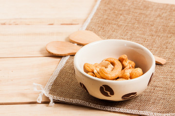 Salted Cashew Nuts in the bowl put on sack and wood background with woodden spoon 