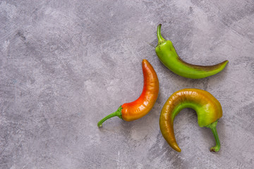 Three green and red peppers on a gray background