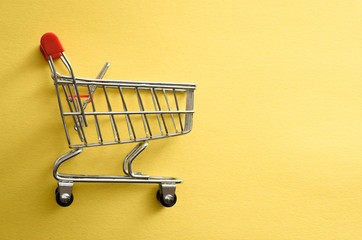 Empty shopping cart over yellow background. Flat lay, top view