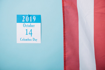 paper calendar with Columbus Day inscription near part of American national flag on blue background
